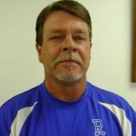 Man in blue shirt with white trim; looking forward, indoors.