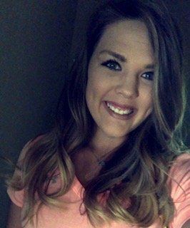 Smiling woman with wavy, ombre hair, wearing a pink shirt.