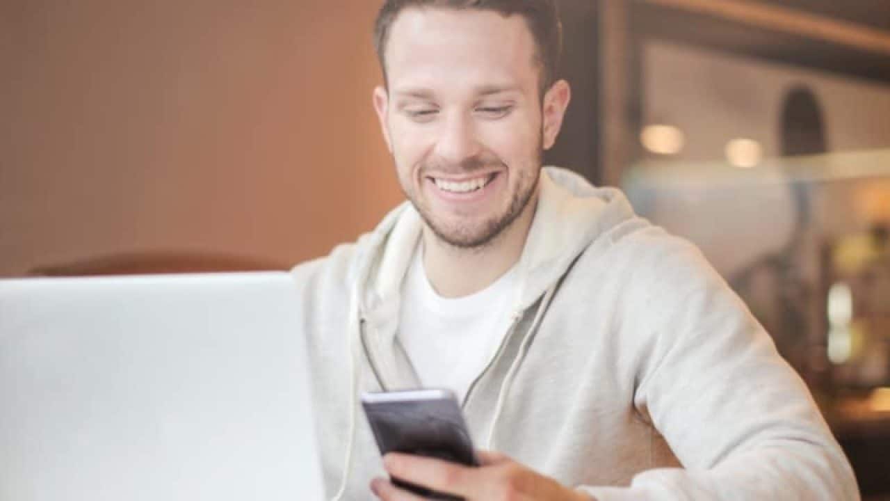 A man is sitting at a table using a laptop and a cell phone.