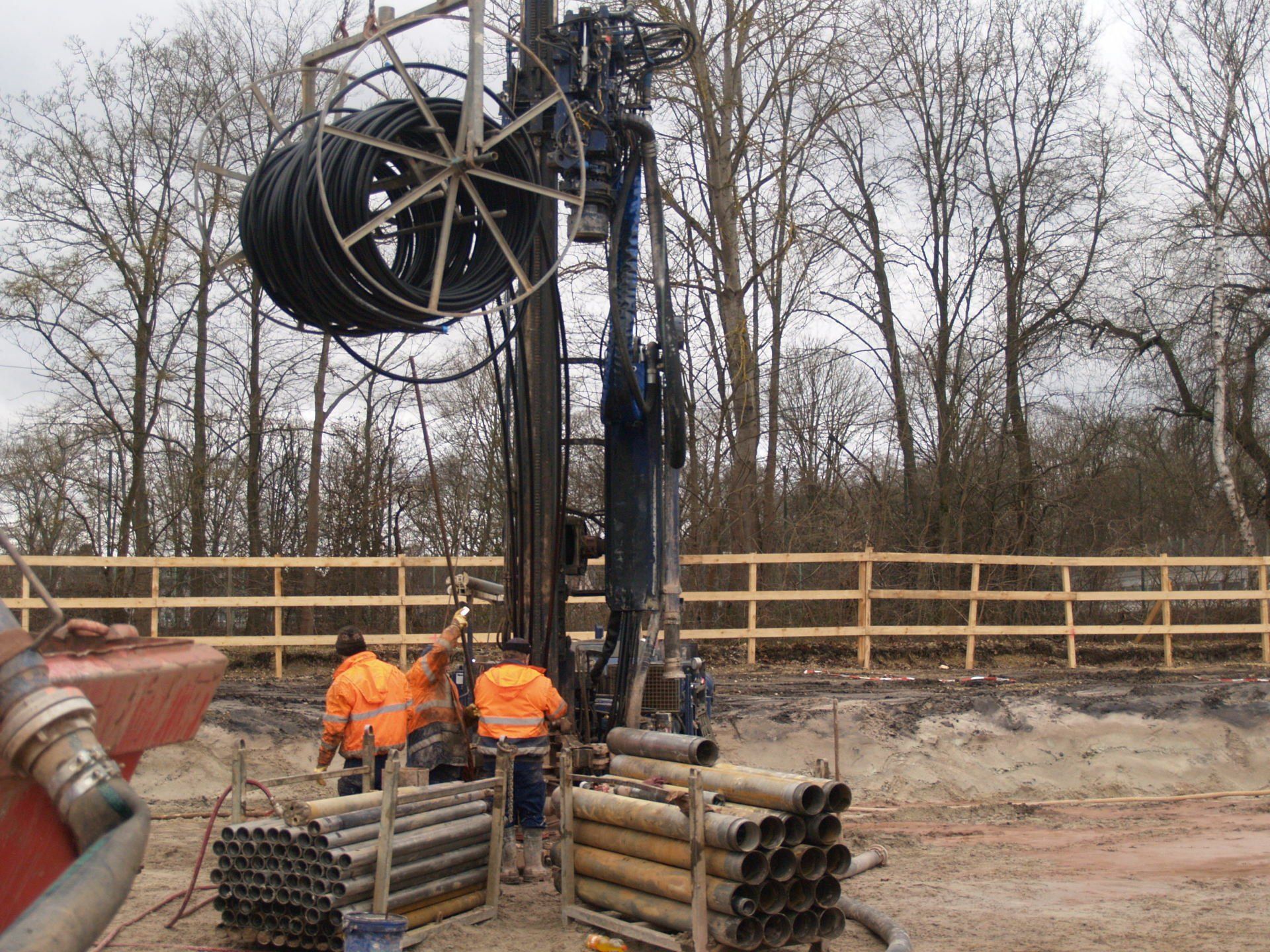 Arbeiter in orangefarbener Schutzkleidung an einer Bohranlage auf einer schlammigen Baustelle