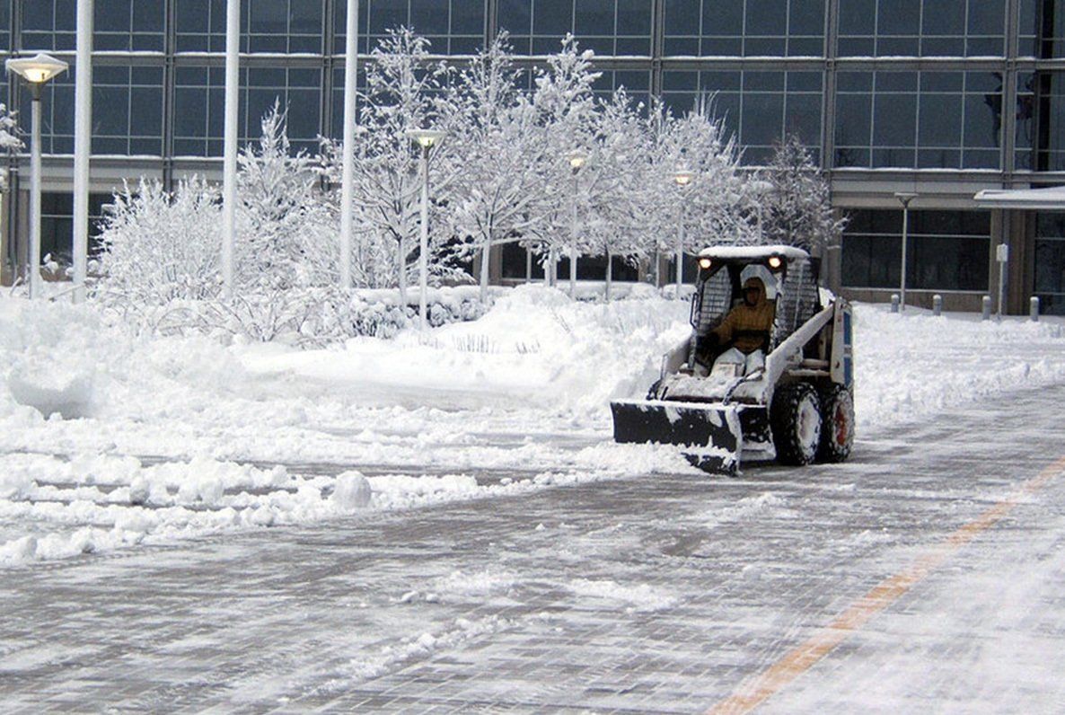 A snow plow is clearing snow from a parking lot in front of a building.