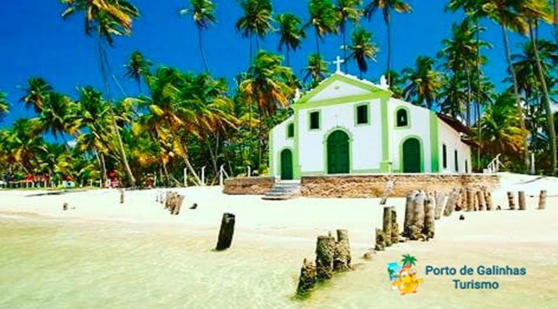Uma igreja verde e branca cercada por palmeiras em uma praia.