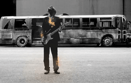 A man is playing a guitar in front of a bus