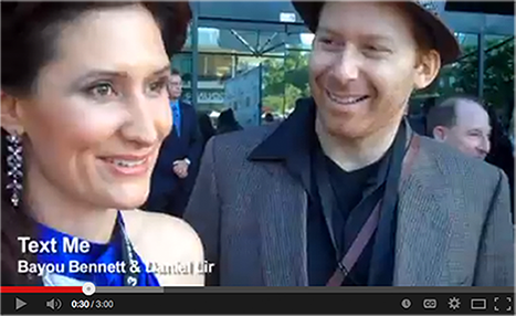 A man and a woman are smiling in a video that says text me