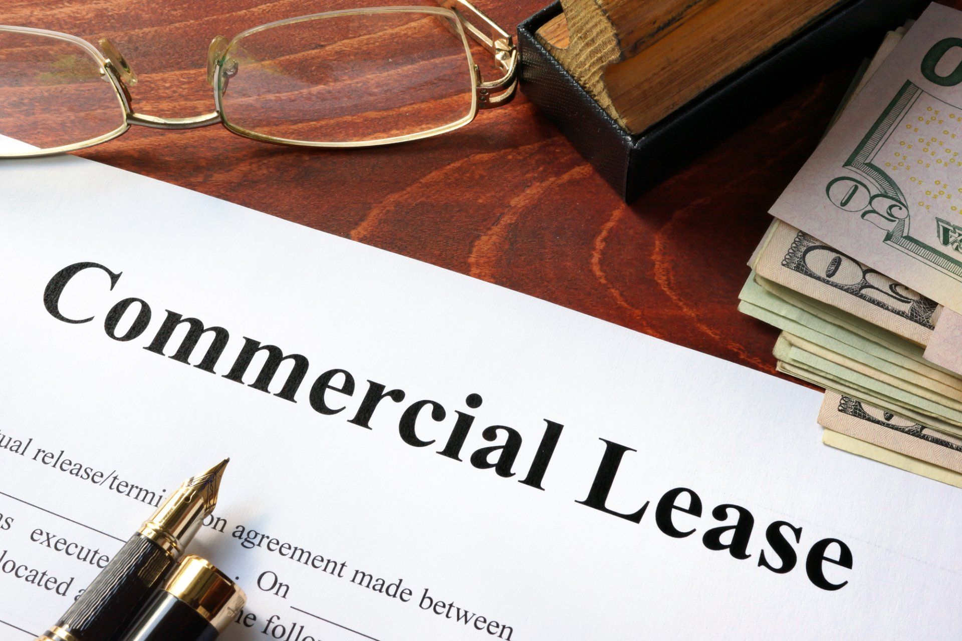 Commercial lease document with glasses, pen, cash, and a wooden stamp holder on a brown surface.