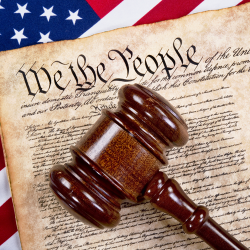 Gavel on the U.S. Constitution with American flag backdrop.