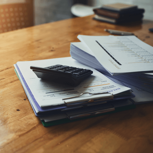 Calculator on documents, stacked on a wooden table, possibly accounting or finance related.