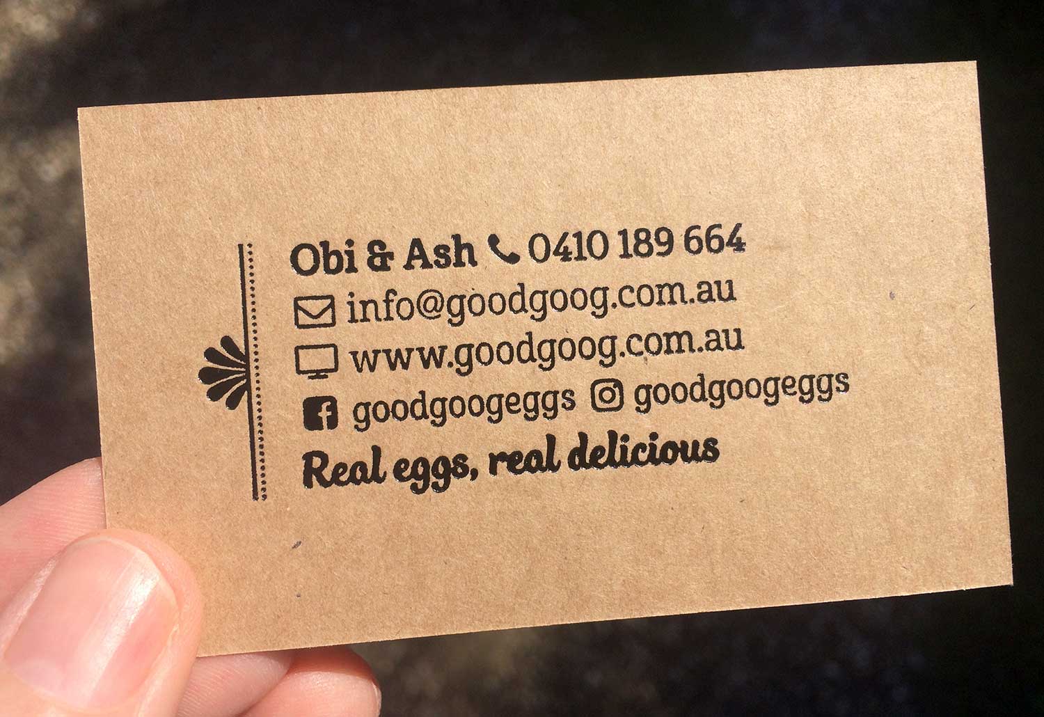 A person is holding a Good Goog business card with the contact details displayed