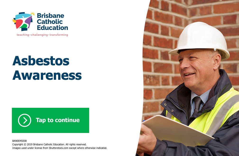 A man wearing a hard hat is holding a clipboard in front of a brick wall.
