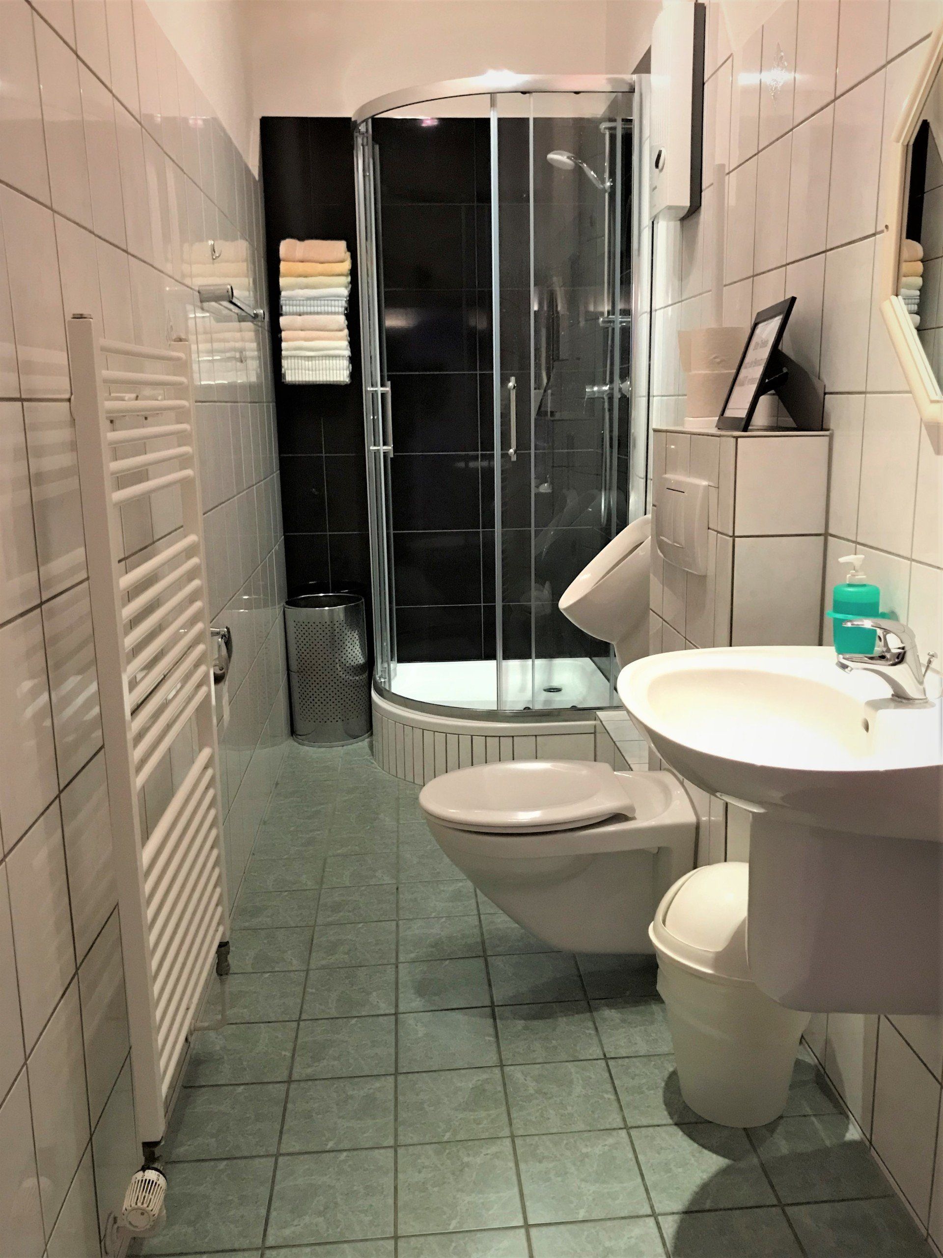 Badezimmer mit Dusche, WC und Waschbecken. Weiße Fliesenwände. Grüner Fliesenboden.