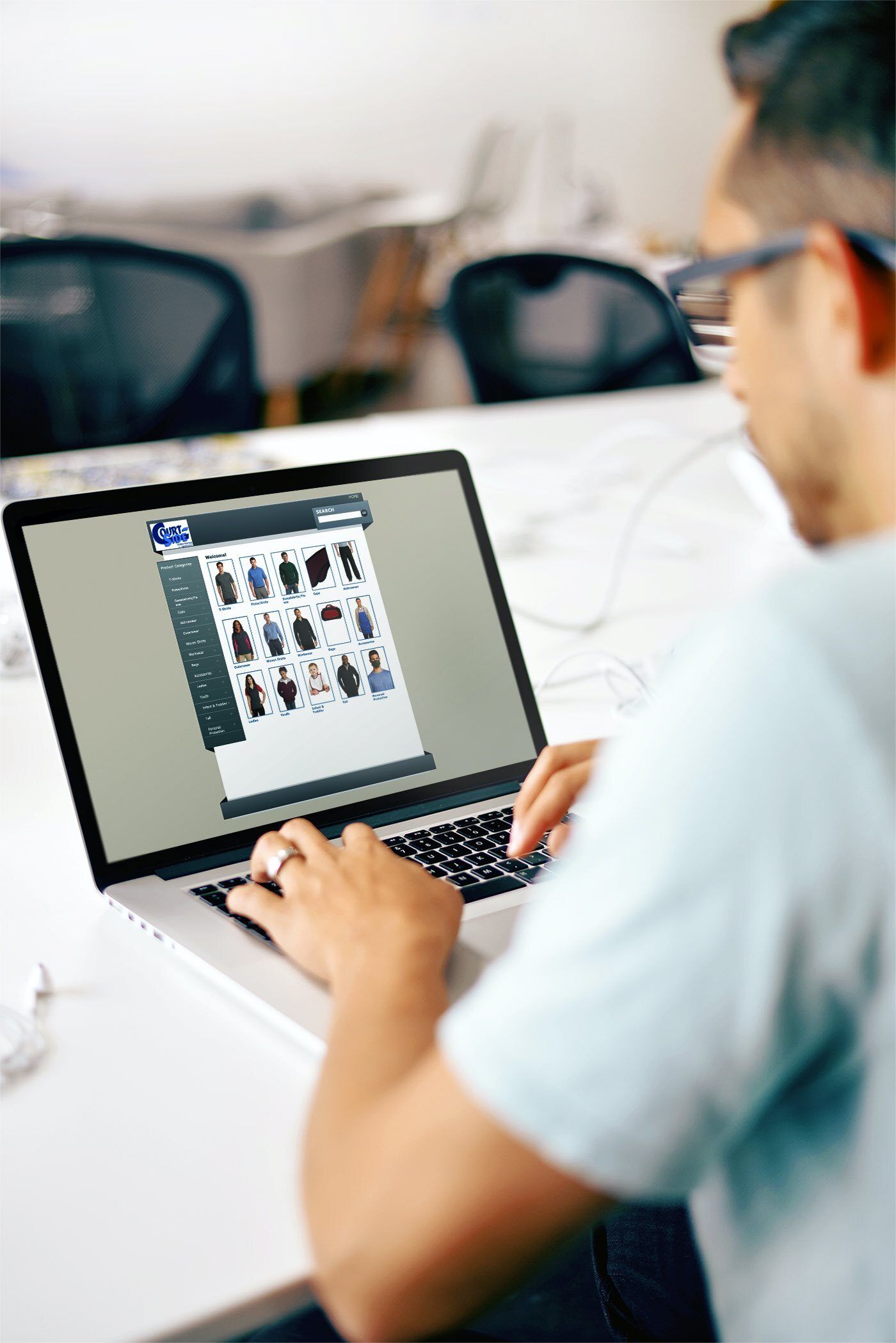 A person sitting at a desk and working on a laptop displaying a website with various clothing product icons.
