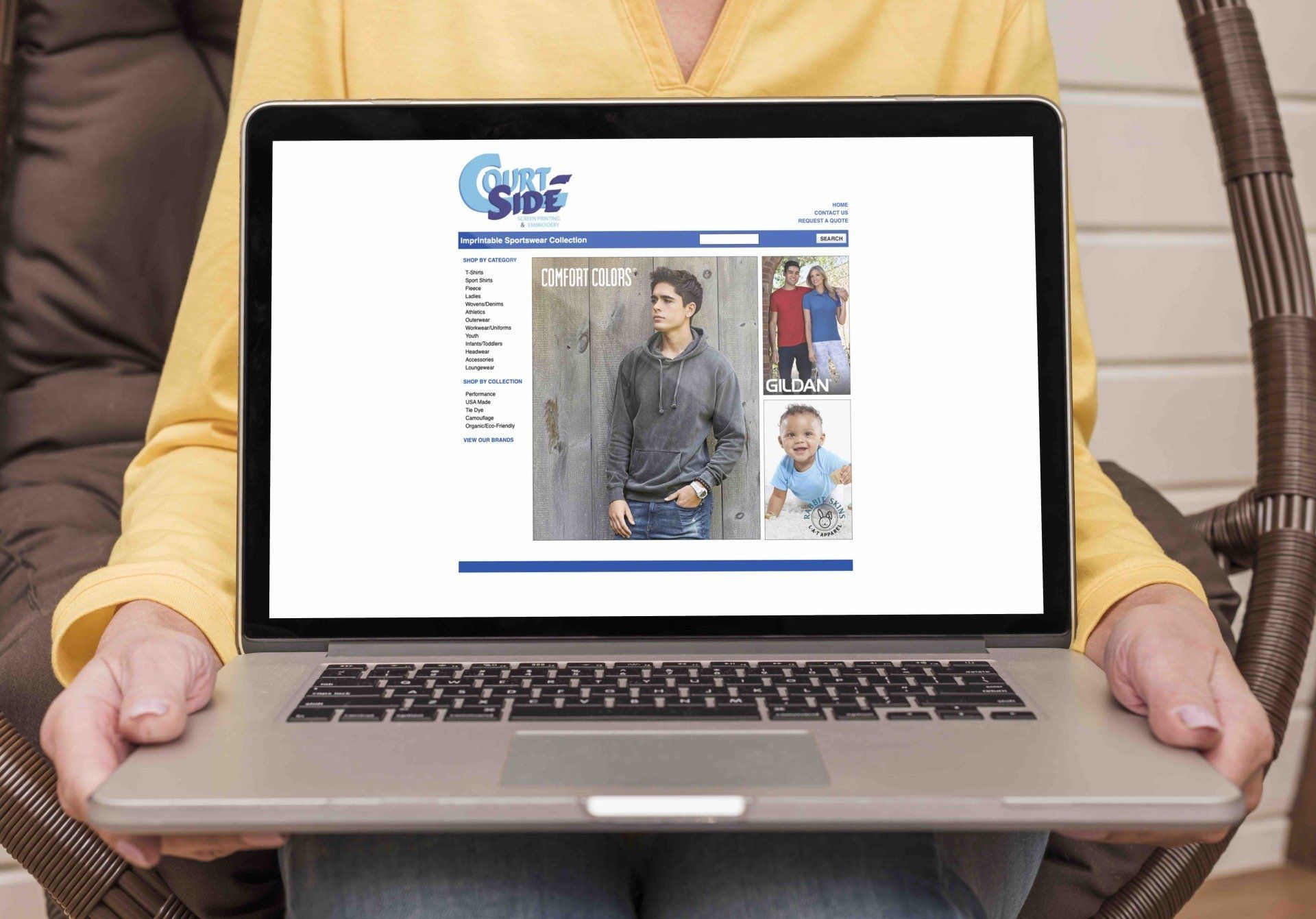 A person sits in a chair holding a laptop displaying a website for a clothing brand called Courtside Apparel.