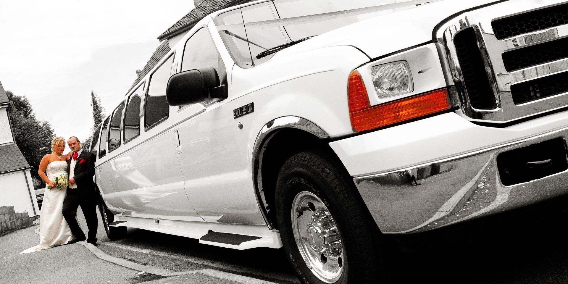 A bride and groom pose in front of a white limousine