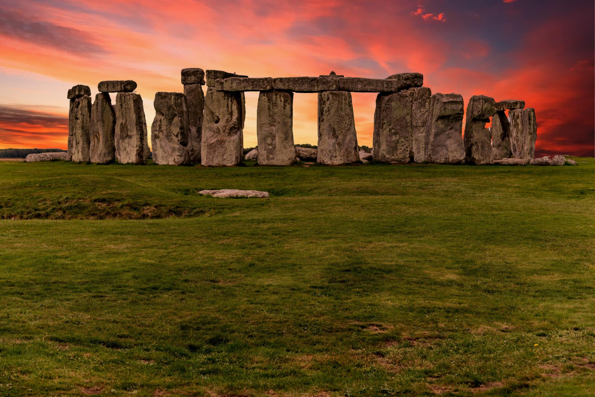 A row of stone pillars in a grassy field with a sunset in the background.
