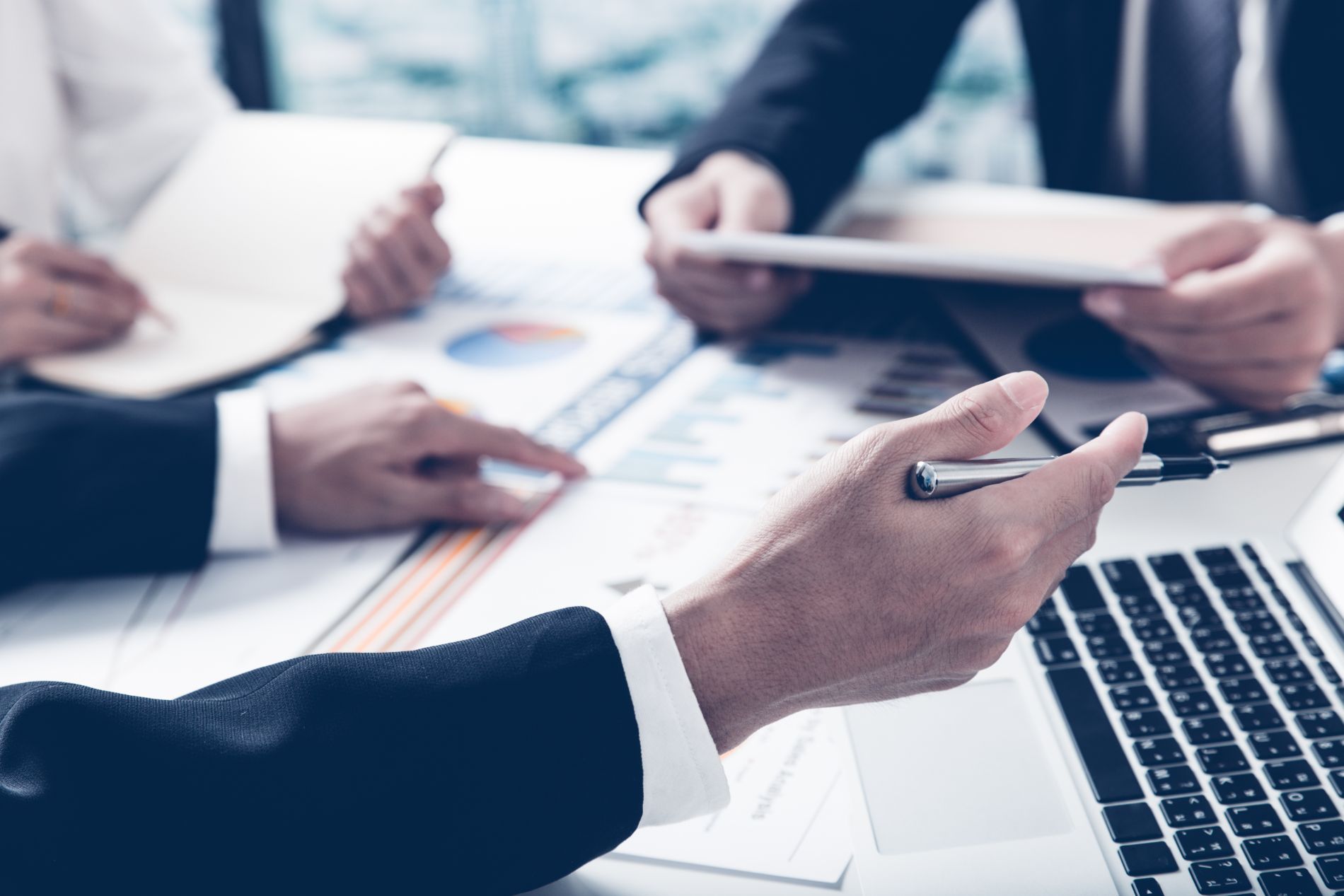Businesspeople analyze charts and graphs during a meeting, pointing at data with a laptop open.