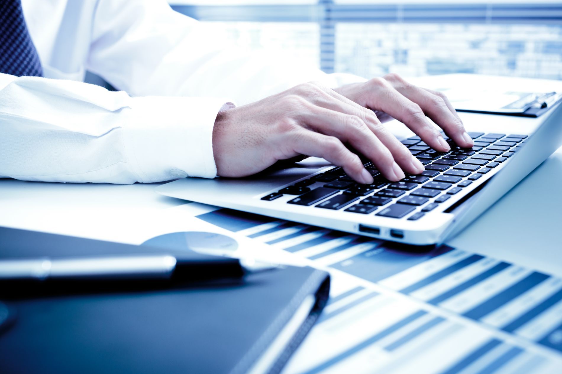 Person typing on laptop over financial charts.