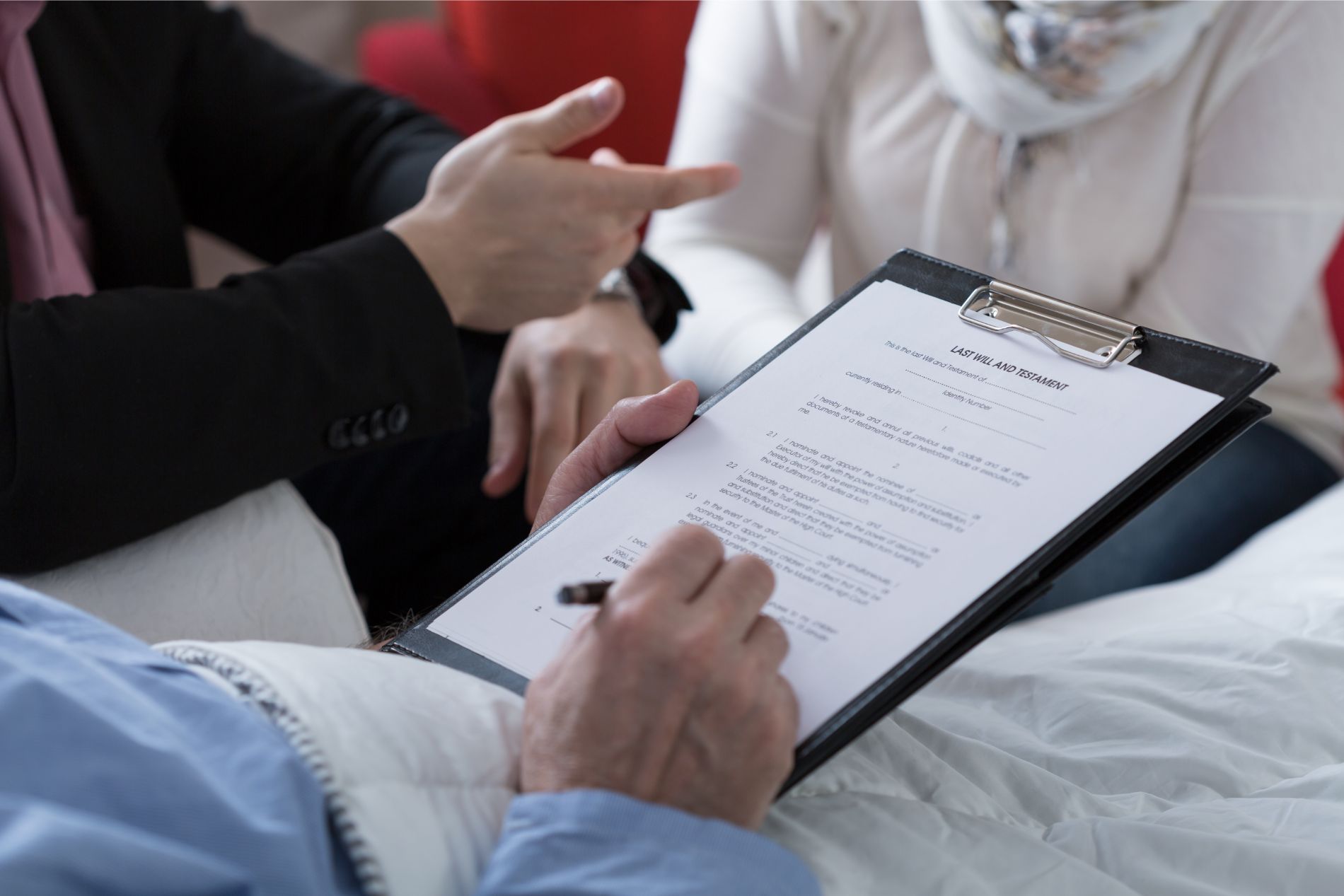 Person signing document on a clipboard, assisted by others in a clinical setting.