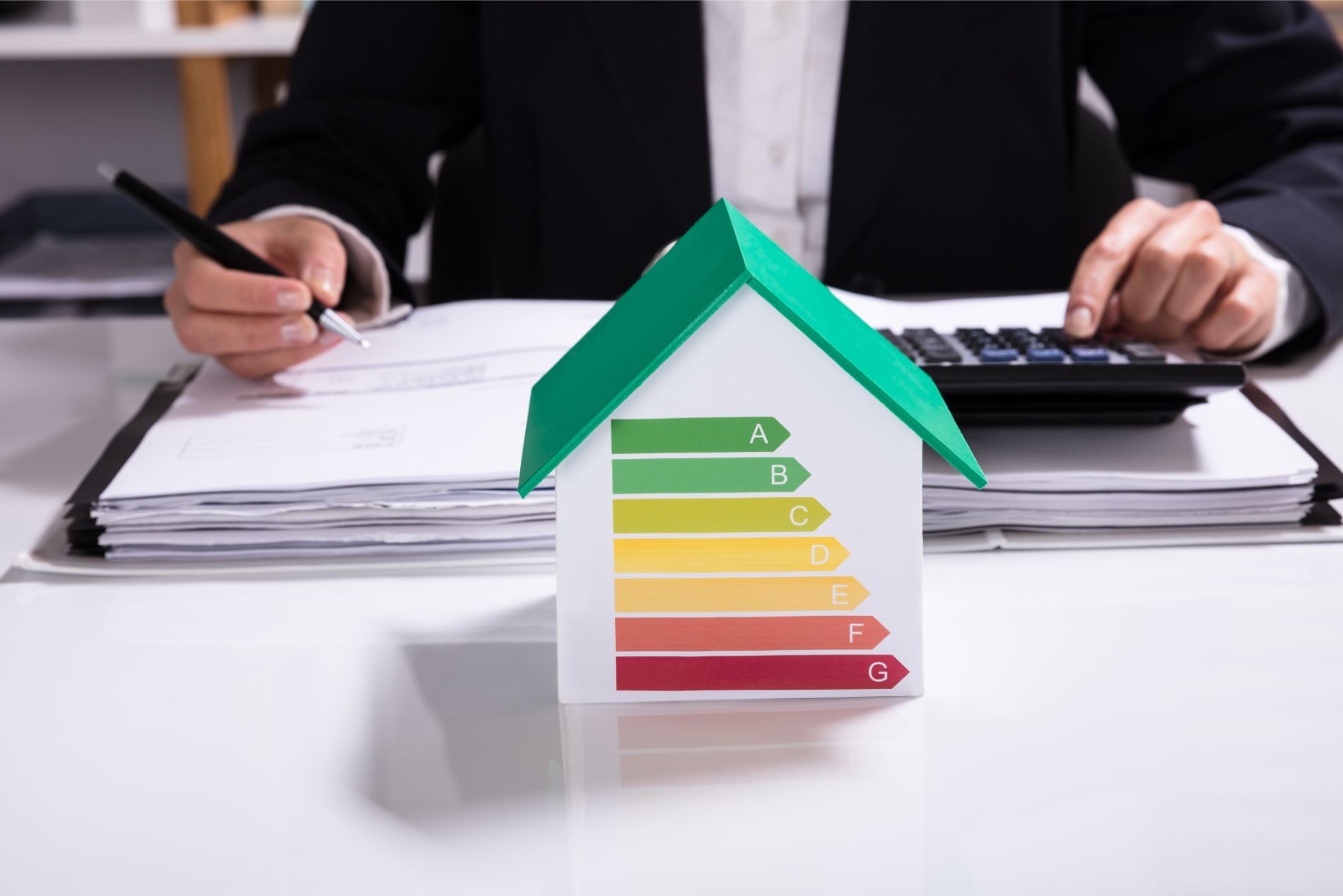 Person using calculator next to a house model with an energy efficiency label.
