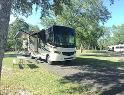 RV parked in a grassy campsite with an awning extended, trees in the background.