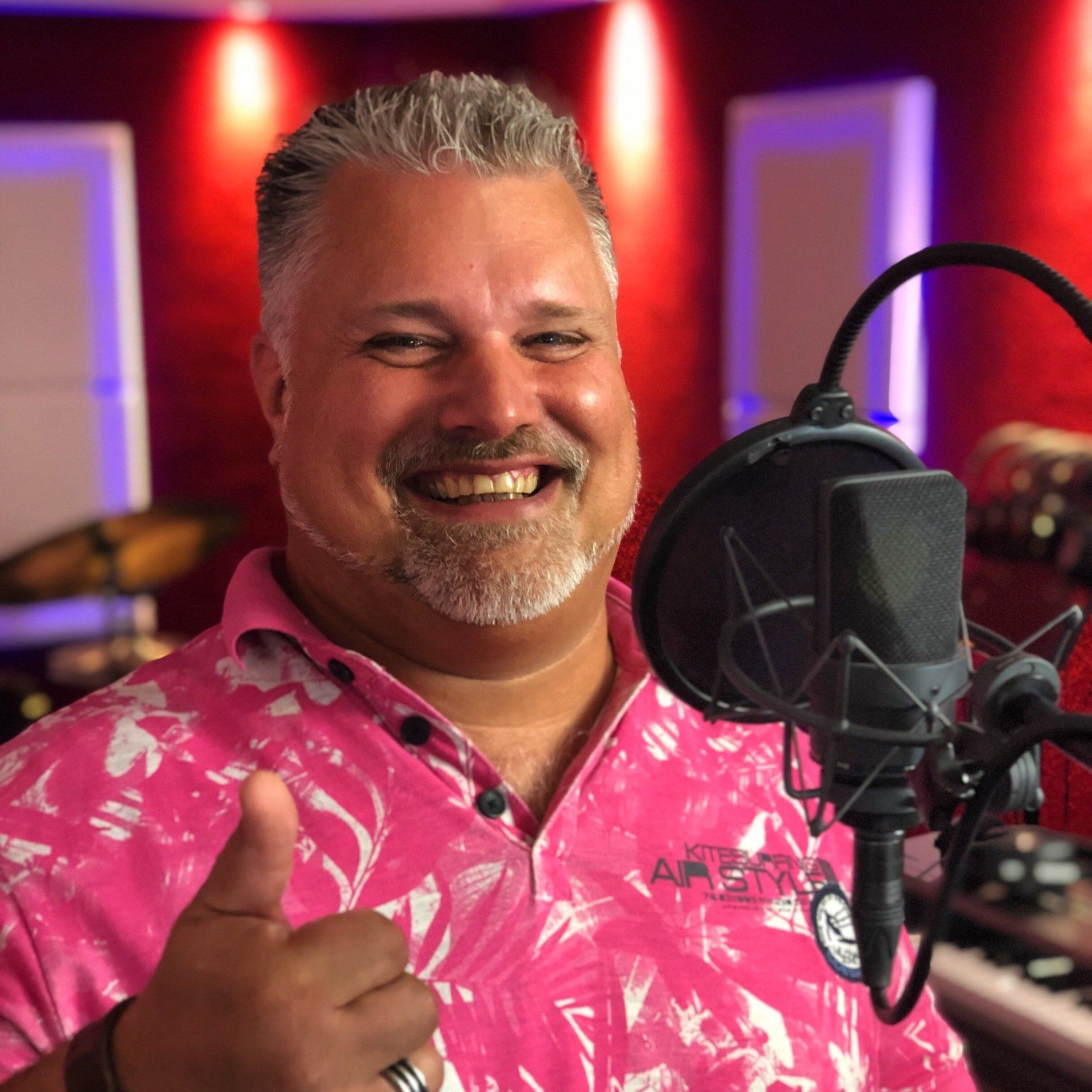 Een man in een roze shirt steekt zijn duim omhoog voor een microfoon