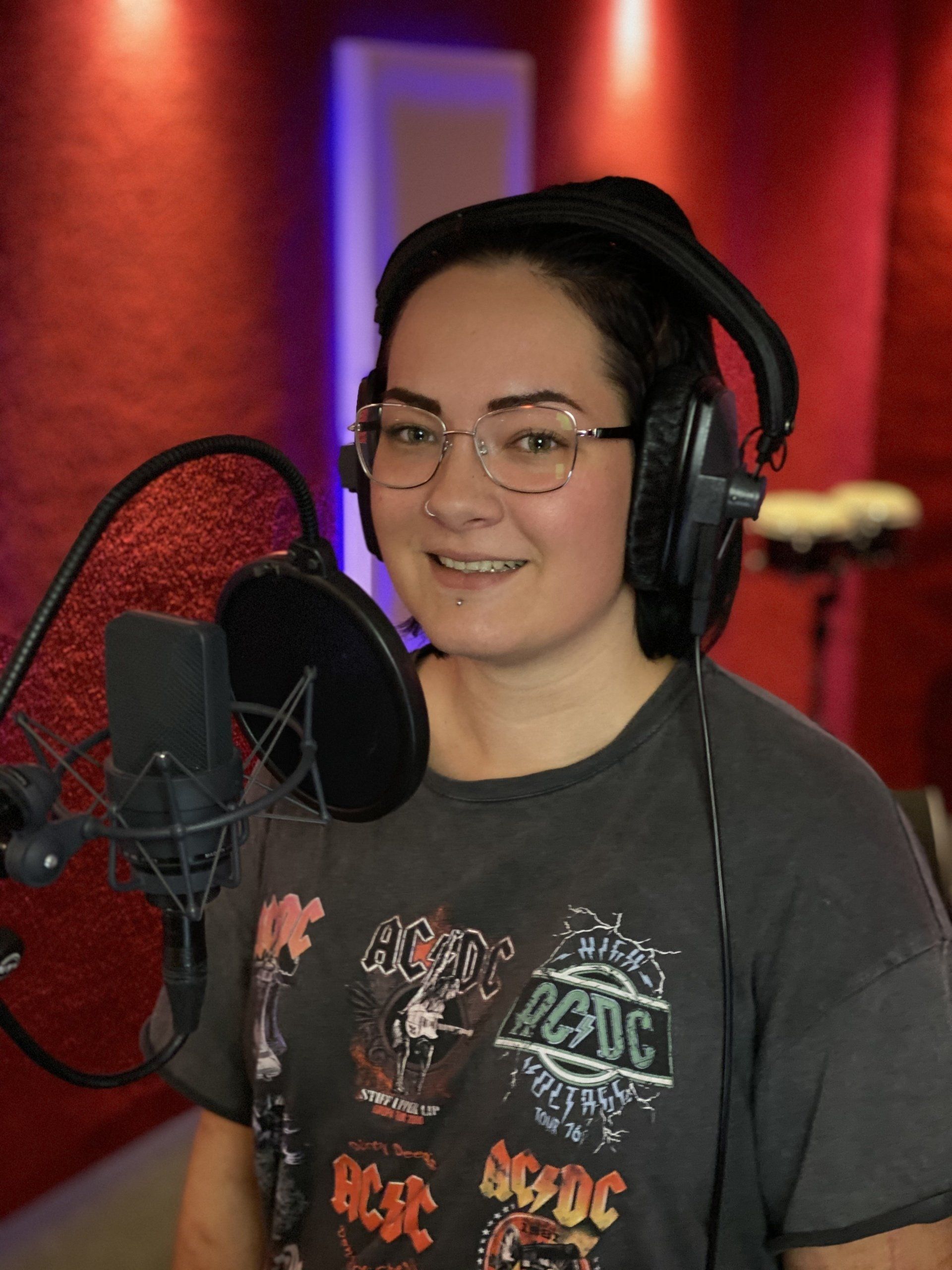 Een vrouw met een koptelefoon en een AC DC-shirt staat voor een microfoon