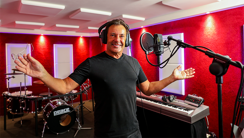 Een man met een koptelefoon staat voor een microfoon in een opnamestudio.