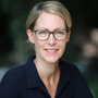 Woman with short blonde hair and glasses smiles outdoors.