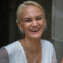 Woman in white lace top, smiling widely, wearing jewelry.