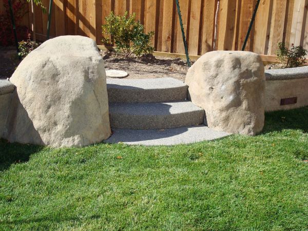 Two large rocks are sitting on top of a lush green lawn next to stairs.