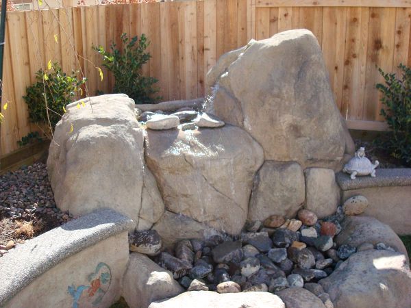 A turtle is sitting on a rock in front of a wooden fence.