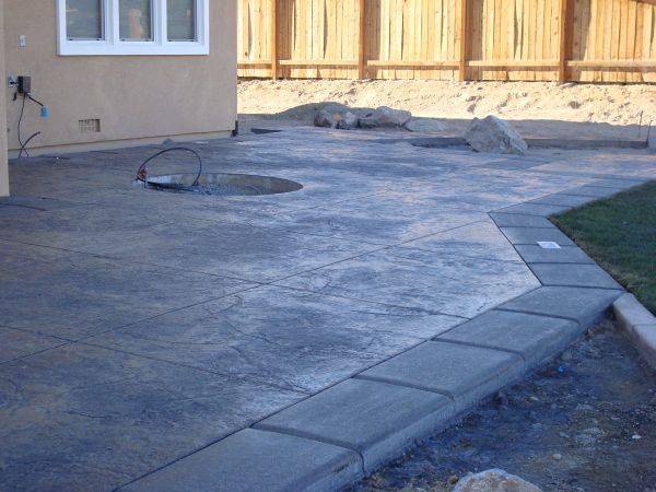 A concrete walkway leading to a house with a wooden fence in the background