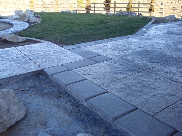 A patio with a walkway and a fence in the background.