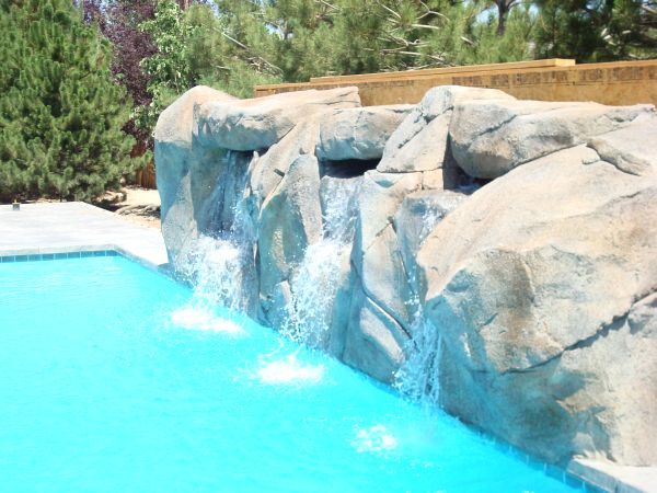 A waterfall is surrounded by rocks next to a swimming pool.