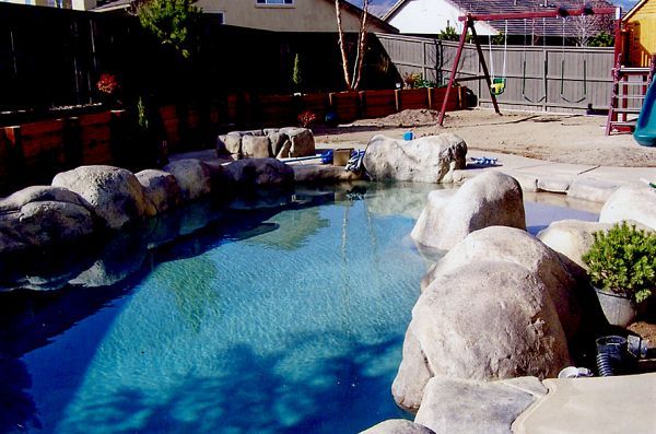 A large swimming pool surrounded by rocks in a backyard