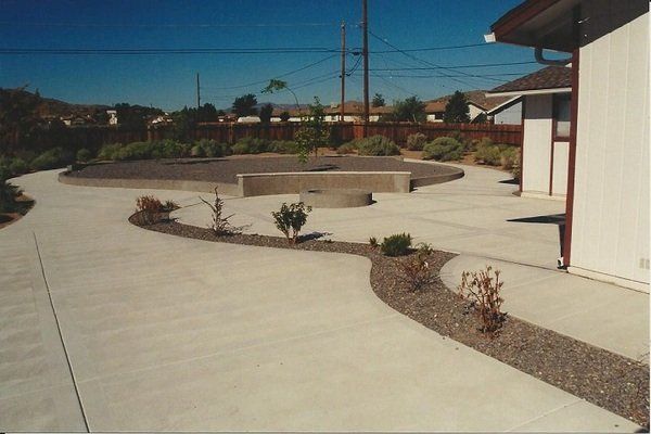 A concrete driveway leading to a house with a pool in the background
