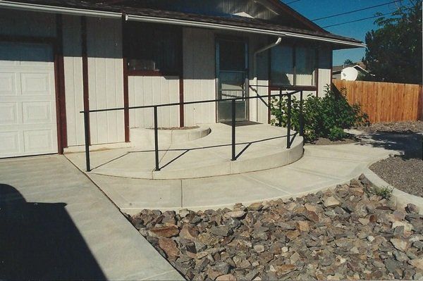 A concrete walkway leading to a house with a metal railing