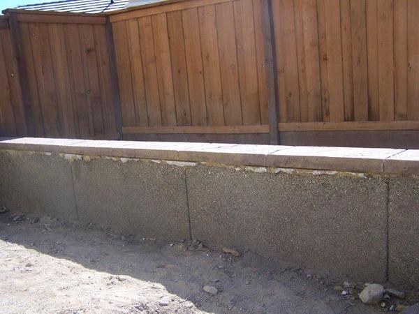 A wooden fence is behind a concrete wall.