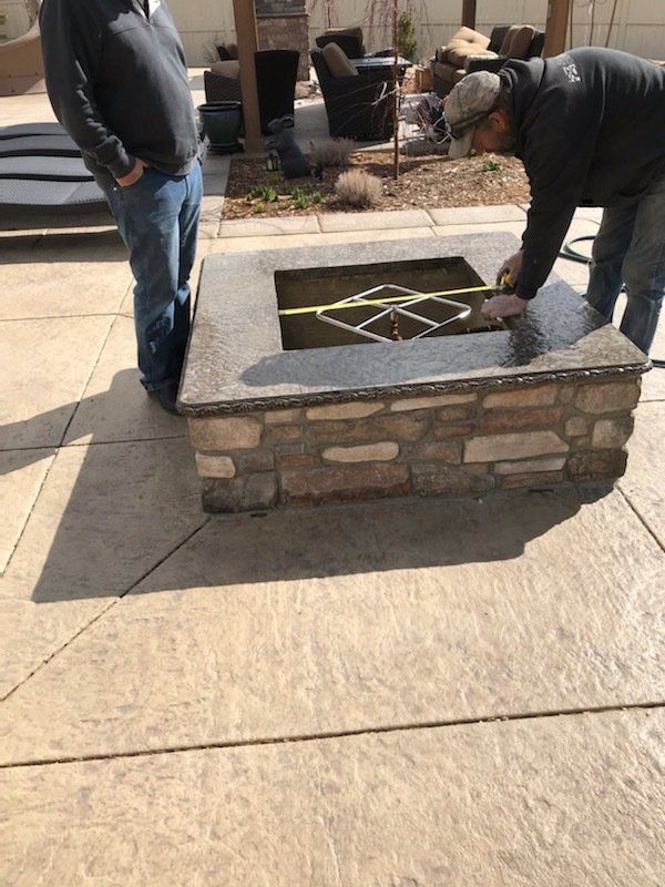 Two men are measuring a fire pit with a tape measure.