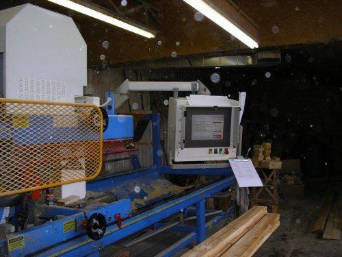 Machine industrielle bleue et blanche dans un atelier, avec un écran d'ordinateur et des planches de bois.