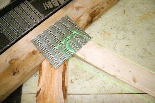 Poutres en bois assemblées par une plaque de connexion métallique, niveau laser vert visible.