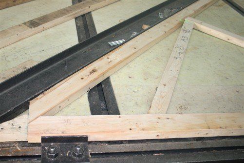 Gros plan sur la charpente d'un toit en bois, avec poutre métallique et supports en bois.