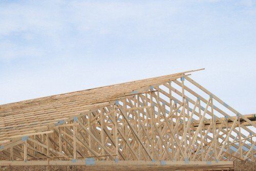 Charpente de toit en bois en construction, sous un ciel partiellement nuageux.
