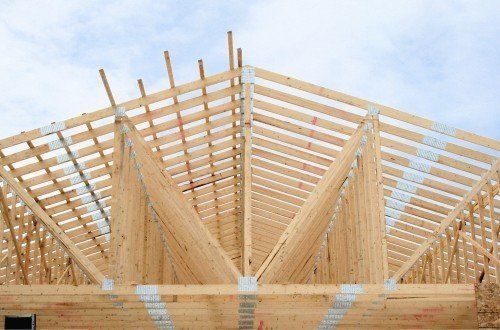 Charpente de toit en bois en construction, sous un ciel nuageux.