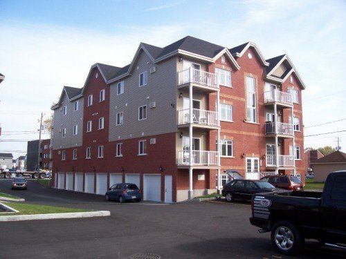 Immeuble d'appartements avec façade en briques et bardage beige, avec garages au rez-de-chaussée. Voitures garées devant.