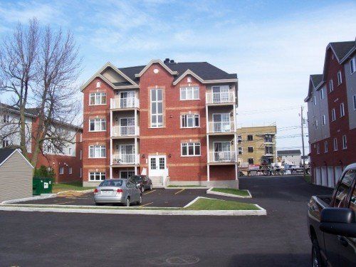 Immeuble d'appartements en briques rouges avec balcons, parking et aire de stationnement pavée.