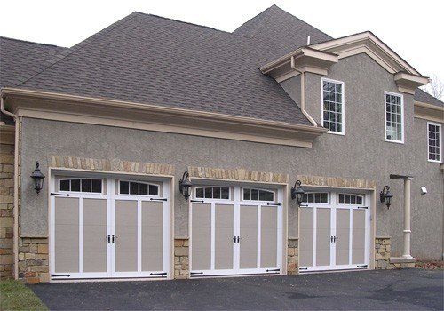 Garage triple avec portes beiges, moulures blanches et accents de pierre sur une maison en stuc.