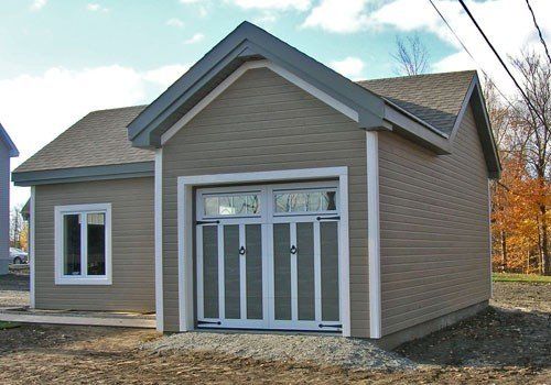 Garage beige avec porte et fenêtre à cadre blanc. Allée en gravier.