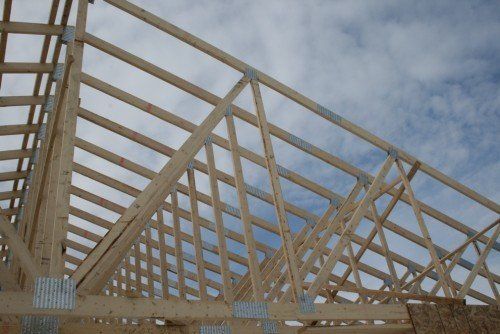 Charpente de toit en bois se détachant sur un ciel nuageux, révélant la structure de l'ossature d'un bâtiment.