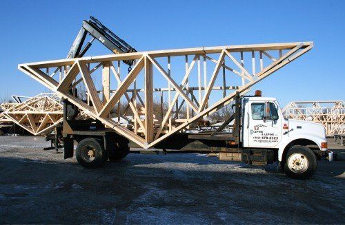 Camion transportant une grande charpente de toit en bois, ciel bleu en arrière-plan.