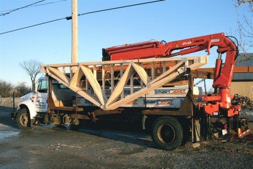 Camion équipé d'une grue rouge soutenant une grande charpente de toit en bois.